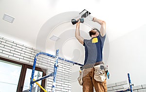 Electrician Builder at work, installation of lamps at height. Professional in overalls with a drill. On the background of the
