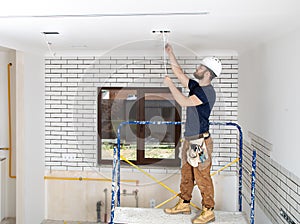 Electrician Builder at work, installation of lamps at height. Professional in overalls with an electrical tool. On the background