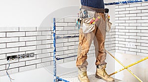 Electrician Builder at work, installation of lamps at height. Professional in overalls with an electrical tool. On the background