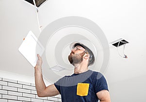 Electrician Builder at work, installation of lamps at height. Professional in overalls with an electrical tool. On the background