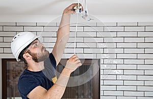 Electrician Builder at work, installation of lamps at height. Professional in overalls with an electrical tool. On the background