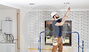 Electrician Builder at work, installation of lamps at height. Professional in overalls with an electrical tool. On the background