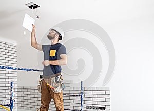 Electrician Builder at work, installation of lamps at height. Professional in overalls with an electrical tool. On the background