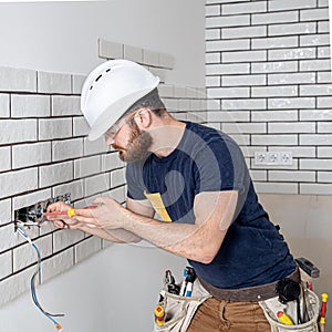 Electrician Builder at work, installation of sockets and switches. Professional in overalls with an electrician`s tool. Against