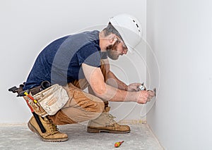 Electrician Builder at work, installation of sockets and switches. Professional in overalls with an electrician`s tool. Against