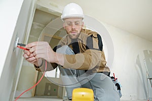 Electrician checking socket voltage using multimeter in wall fixture