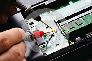 Electrician checks electronic circuit board by probe of digital multimeter.