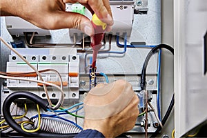 Electrician connects blue wire of power cable to neutral terminal bar in electrical panel during electrical installation