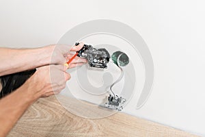 Electrician connects the sockets to the electrical wires on wall in White room. Screwdriver, close-up electrician hands.