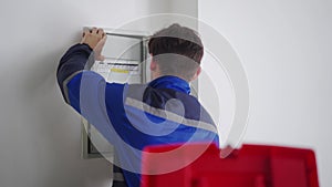 Electrician disassembles electrical fuse box. Master in uniform puts off electrical panel to fix electricity. Repairman