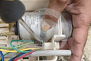 An electrician dismantles the control panel of a window type air conditioner control panel outside