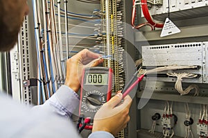 Electrician engineer with multimeter tests electrical control panel of automation equipment. Specialist in the Controller cabinet.