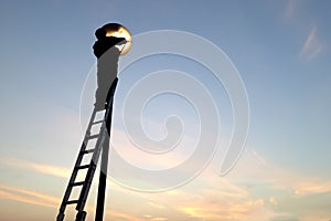 Electrician fixing street light bulbs and climbing on a ladder