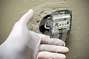 Electrician hands in gloves installing light switch in wall