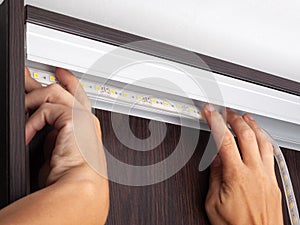 Electrician hands install LED strip lighting  in the niche of the cabinet to illuminate the wardrobe