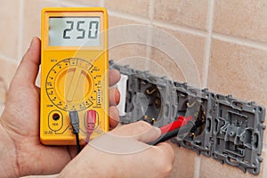 Electrician hands with multimeter measuring the voltage in a wall fixture