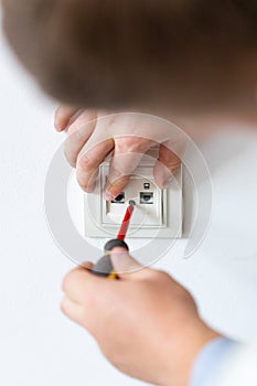 Electrician hands tighten bolts in wall fixture or socket using screwdriver.