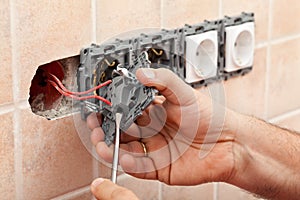 Electrician hands tighten electrical wires in wall fixture or so