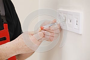 Electrician hands tighten electrical wires in wall fixture or socket using a screw driver - closeup. Installing electrical outlet