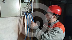 An electrician in a hard hat and face shield inspects the electrical wires.
