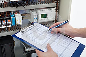 Electrician holding clipboard while examining fusebox