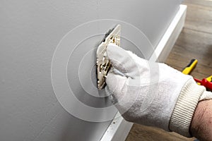 An electrician inserts a double grounded electrical socket into an electrical box in the room wall.