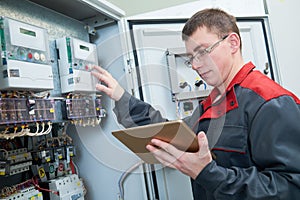 Electrician inspectinf fuse box circuit with tablet computor