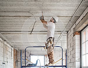 Electrician installer with a tool in his hands, working with cable on the construction site