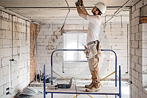 Electrician installer with a tool in his hands, working with cable on the construction site