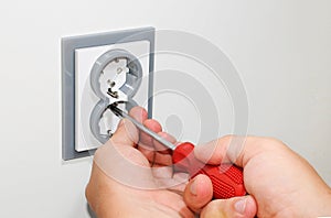 Electrician installing a grey wall-mounted AC power socket with a screwdriver on a white wall, renovating home.