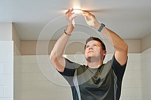 electrician installing lamp on stretch ceiling indoors