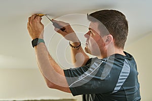 electrician installing lamp on stretch ceiling indoors