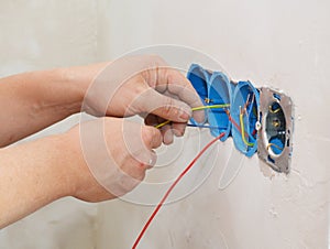 An electrician is installing a new multiple socket electrical outlet installing the wires, cable in the junction box