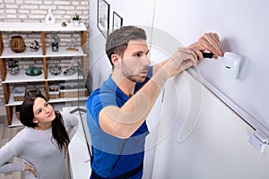 Electrician Installing Security System Motion Detector On Wall