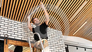 An electrician installs an LED lamp on a wooden plank ceiling. Repair of household electrical networks. Lamp replacement service.