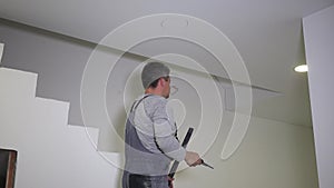 Electrician man with handsaw sawing hole in gypsum ceiling