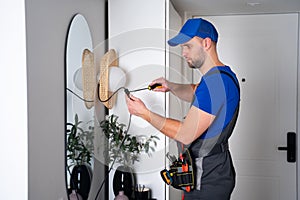 An electrician man in a work uniform repairs a lamp in the corridor.