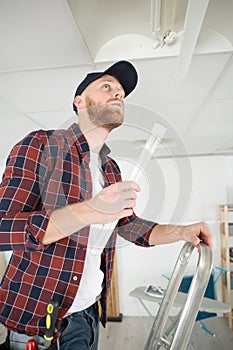 Electrician man worker installing ceiling fluorescent in office