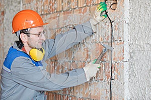 Electrician man worker installing electrical cable at house wall