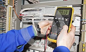 Electrician measures voltage by tester. multimeter is in hands of engineer in electrical cabinet
