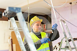 Electrician in protective uniform and helmet with pliers in his hands prepares electrical wiring in house under