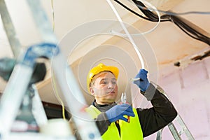 Electrician in protective uniform and helmet with pliers in his hands prepares electrical wiring in house under