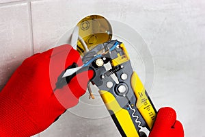 An electrician in red gloves, using wire cutters, remove insulation from electrical wires. Handyman