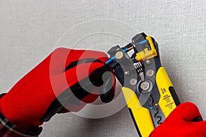 An electrician in red gloves is using wire cutters to remove insulation from electrical wires.