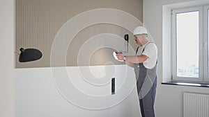 Electrician after repair in a bright modern house checks the work of the wall sconces of the lamp