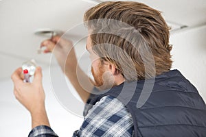 electrician replacing spotlight bulb in ceiling