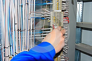 The electrician`s hand carries out wiring to the terminals of the electrical cabinet.