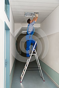 Electrician on stepladder installs lighting to the ceiling