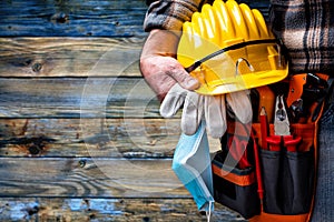 Electrician technician with tool belt and surgical mask on rustic light wood background. Electricity. Covid-19 prevention