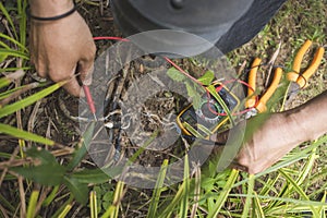 An electrician tests an exposed grounded wire with a digital multimeter with LCD screen. Safety procedure at a home garden
